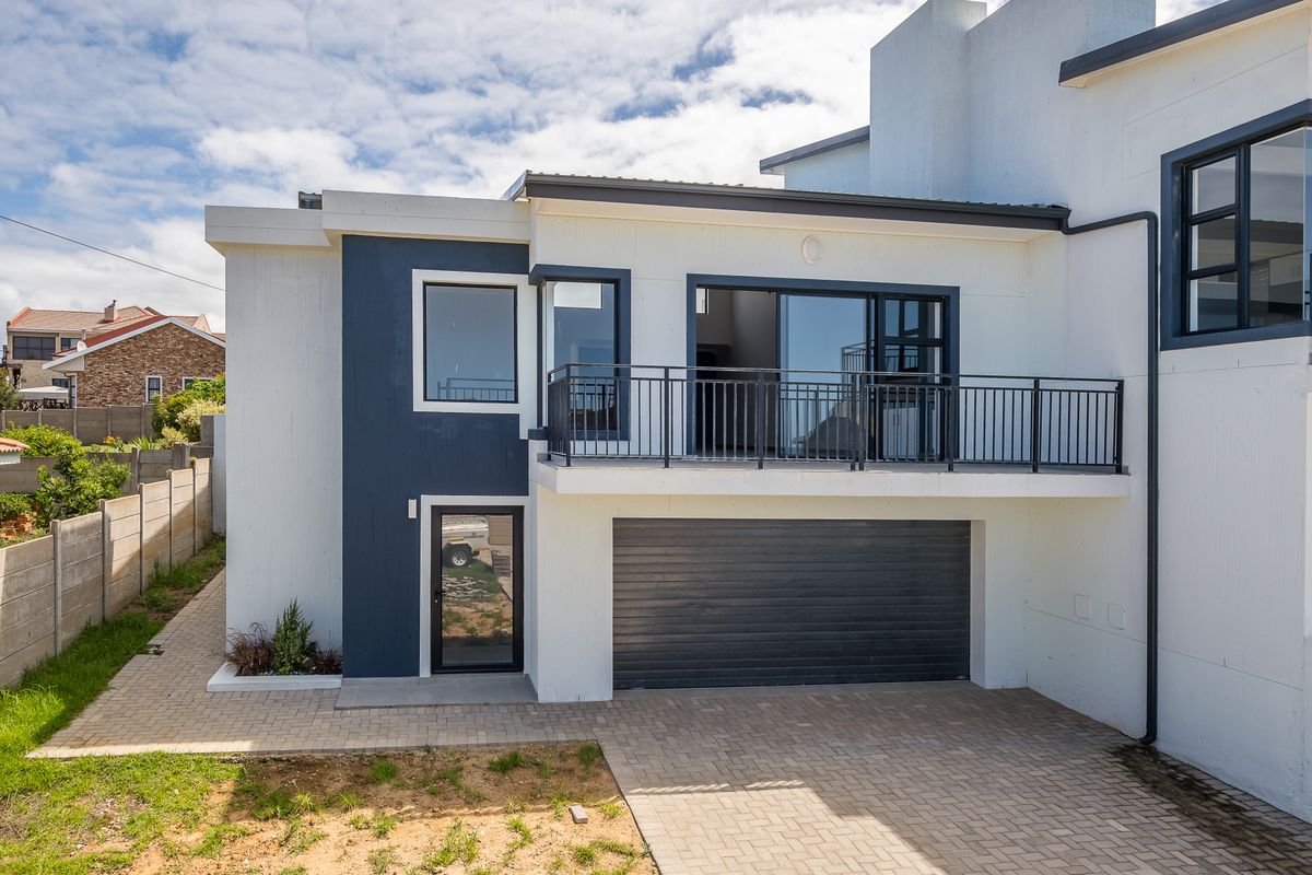 Rear exterior view of a modern duet property featuring a paved driveway, single garage, and an upper-level balcony with metal railings.