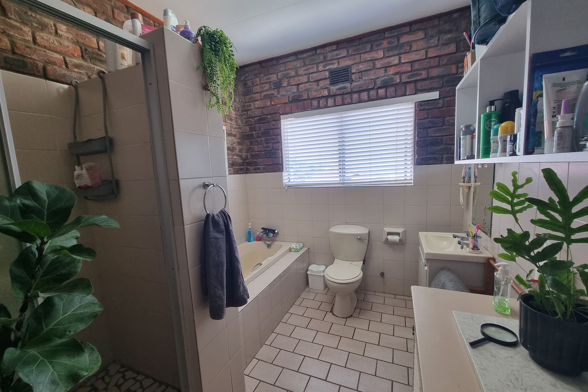 A functional bathroom featuring a built-in bathtub, separate shower enclosure, toilet, and vanity, accented with exposed brick wall detailing.