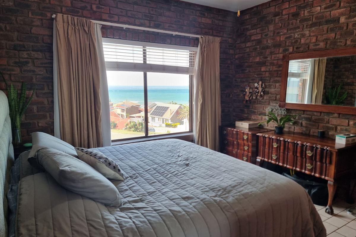 A bedroom featuring exposed brick walls and a large window offering scenic coastal and neighbourhood views.