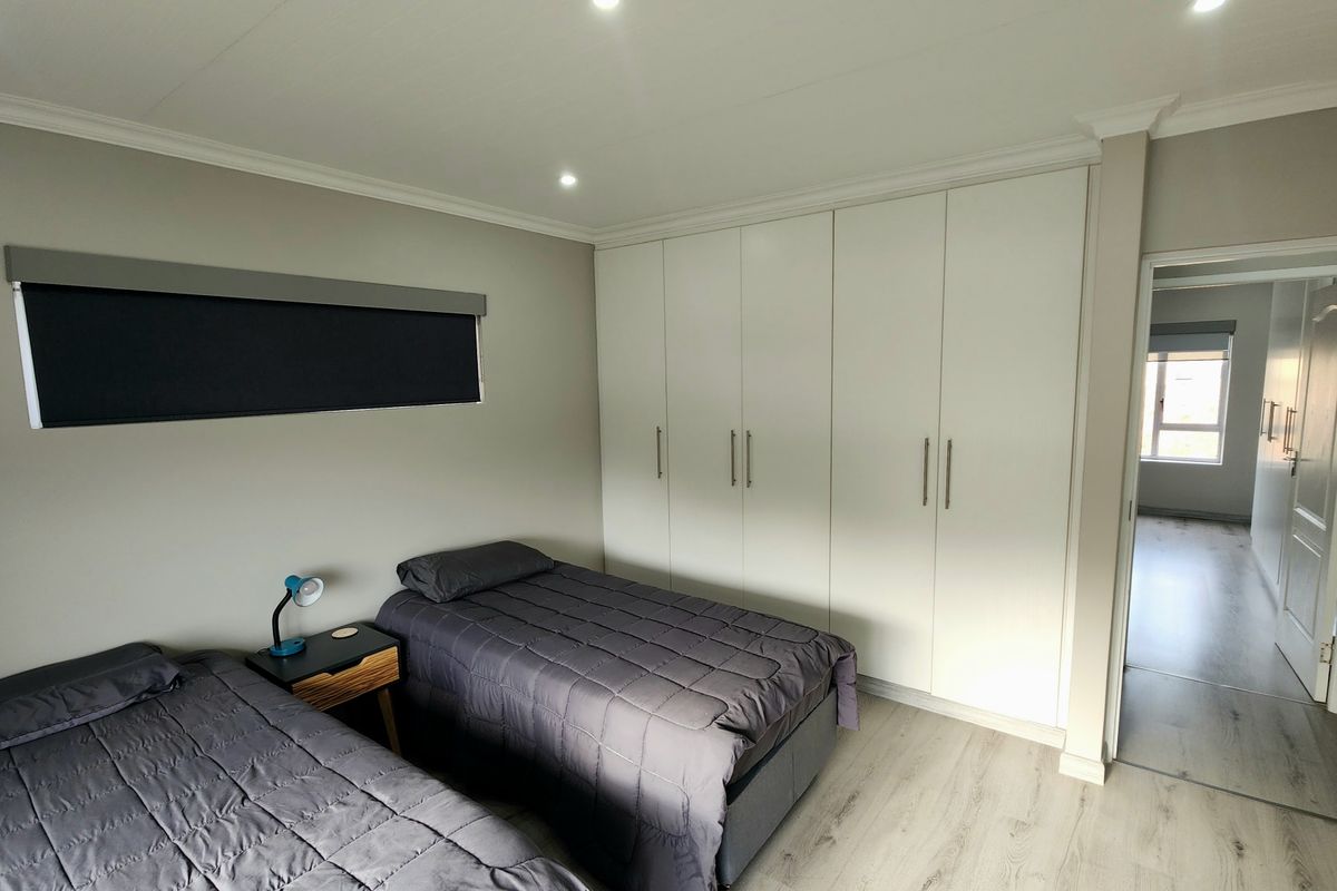 A well-maintained bedroom featuring built-in floor-to-ceiling wardrobes, recessed ceiling lighting, and modern laminate flooring.