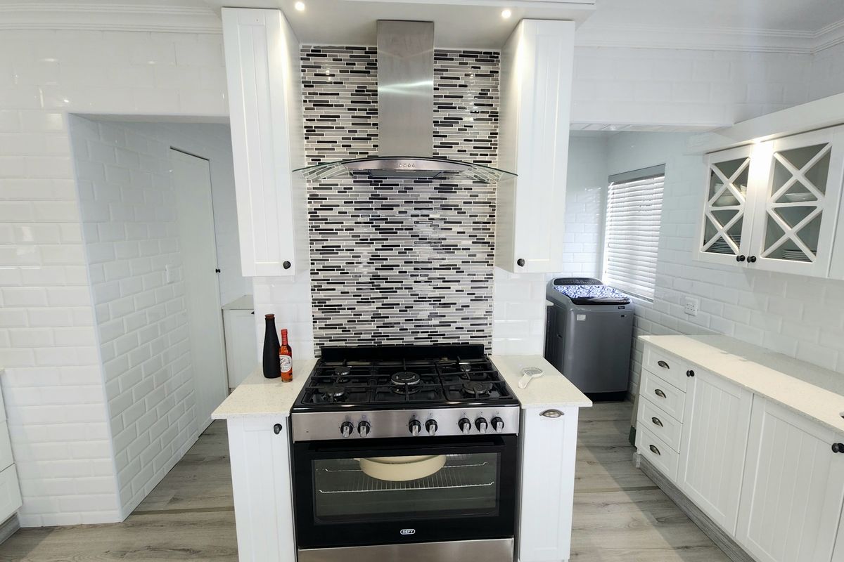 Modern kitchen featuring white cabinetry, subway tile backsplash, stone countertops, and a stainless steel gas stove with a glass extractor fan.