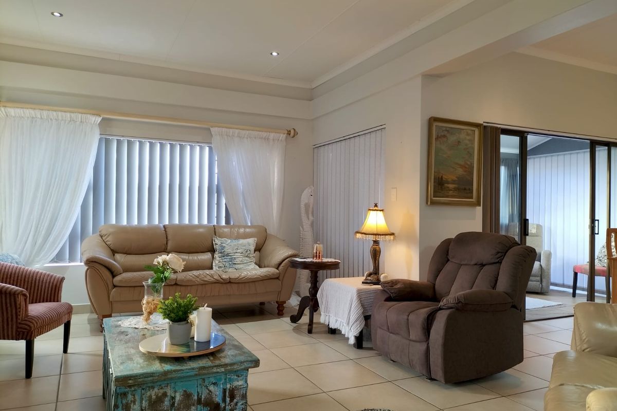 A spacious living room featuring tiled flooring, recessed ceiling lighting, and large windows with vertical blinds, leading to an adjacent patio area.