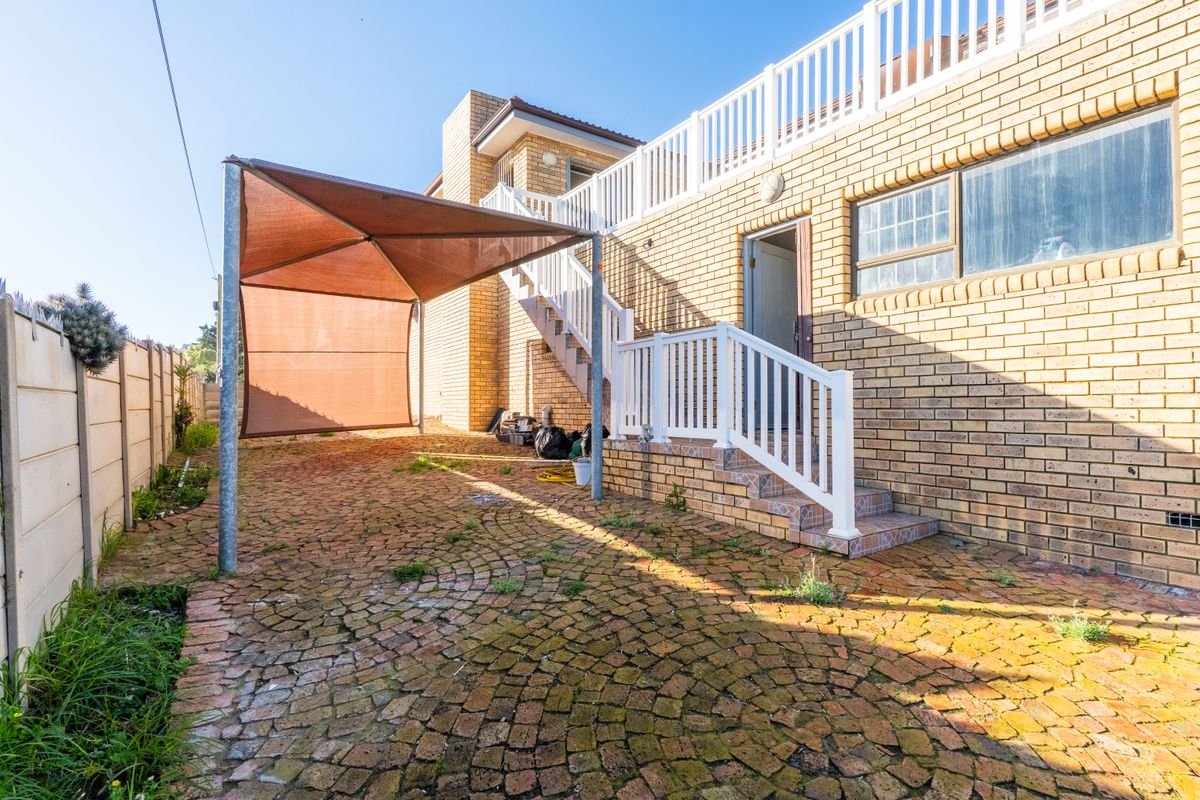 Rear exterior view featuring brick paving, a shade sail structure, and an external staircase leading to an upper level balcony.