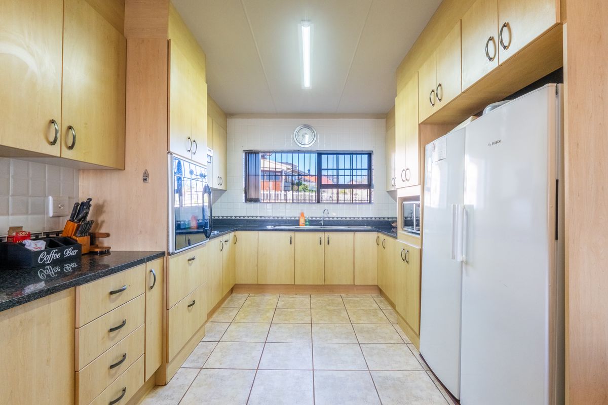 A functional kitchen featuring light wood-toned cabinetry, dark laminate countertops, tiled flooring, and a built-in oven with a window overlooking the exterior.