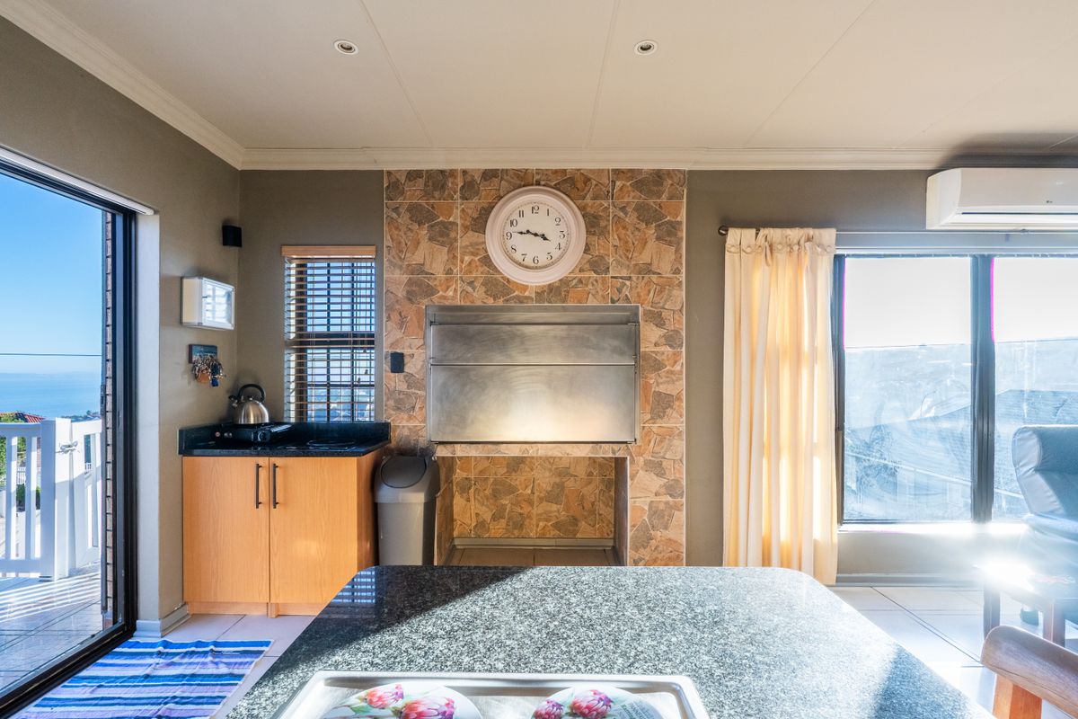 Living area featuring a built-in braai with stone tile surround, granite countertop, built-in cabinetry, and direct access to an outdoor balcony with sea views.