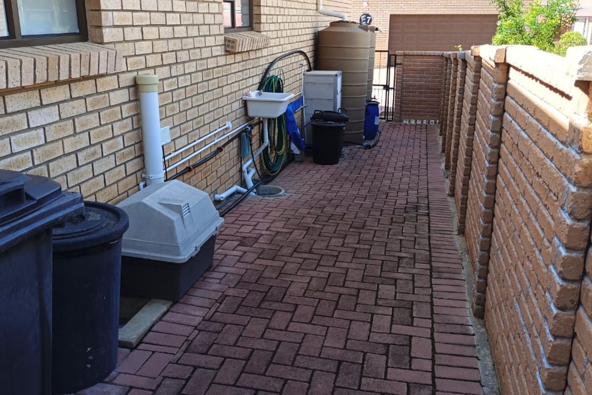 A side exterior walkway featuring brick paving, a boundary wall, a utility sink, and a water storage tank.