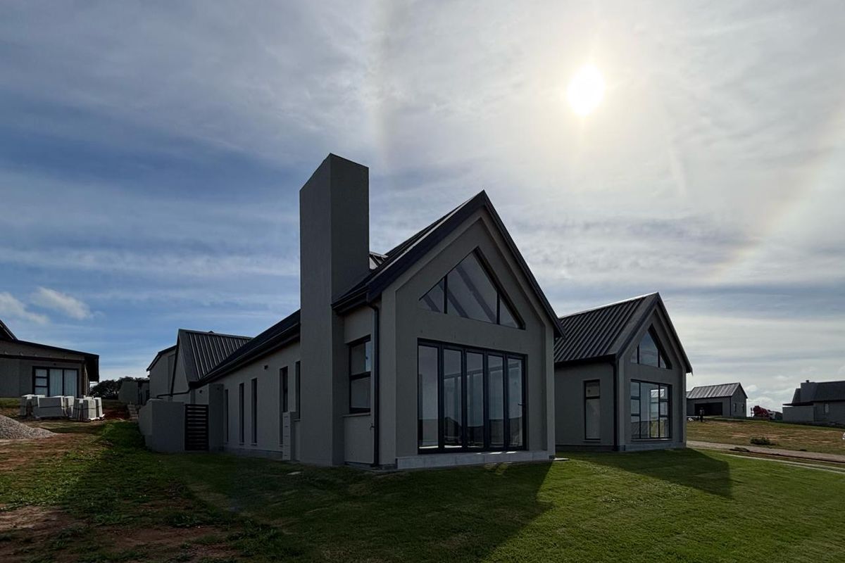 Modern architectural house exterior featuring a pitched roof, large glass windows, and a prominent chimney, set within a landscaped estate environment.