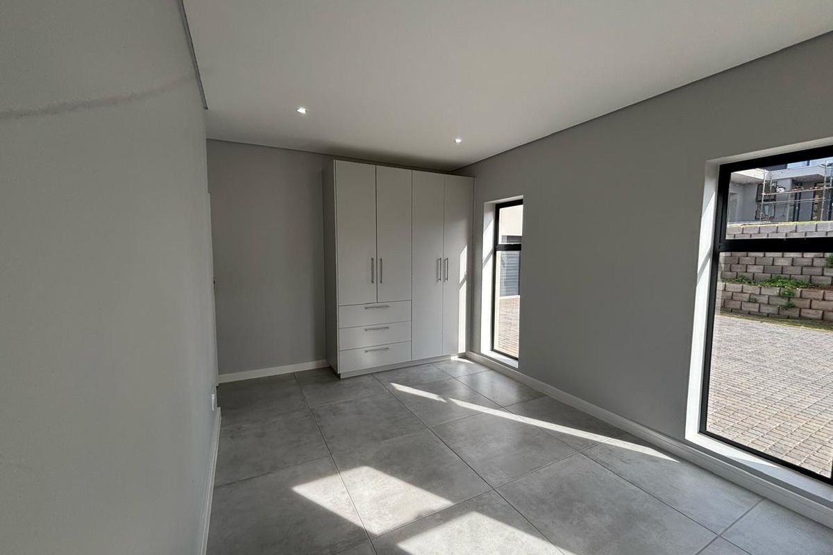 A bright, modern bedroom featuring large format floor tiles, recessed ceiling lighting, and built-in cabinetry with a clean, minimalist aesthetic.