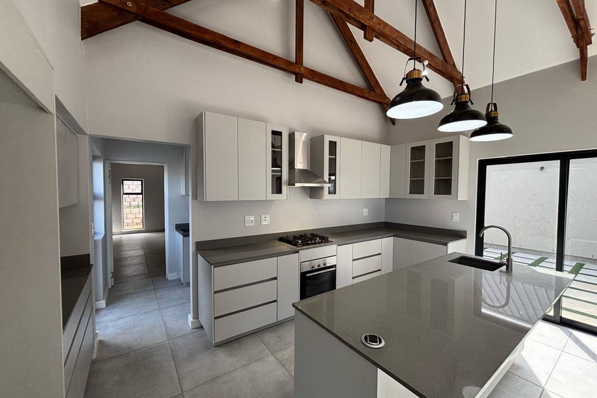 Modern kitchen featuring a central island, stone countertops, built-in oven, gas hob, extractor fan, and exposed timber roof trusses.