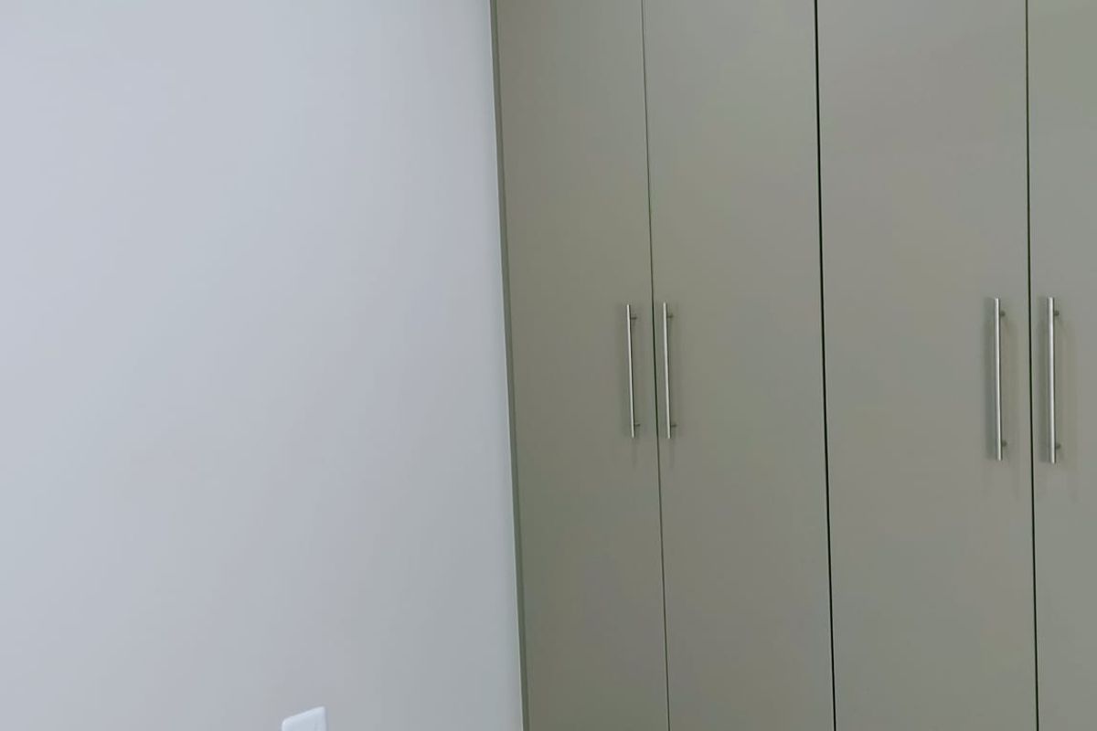 A clean bedroom interior featuring modern built-in cupboards with sleek handles and neutral floor tiling.