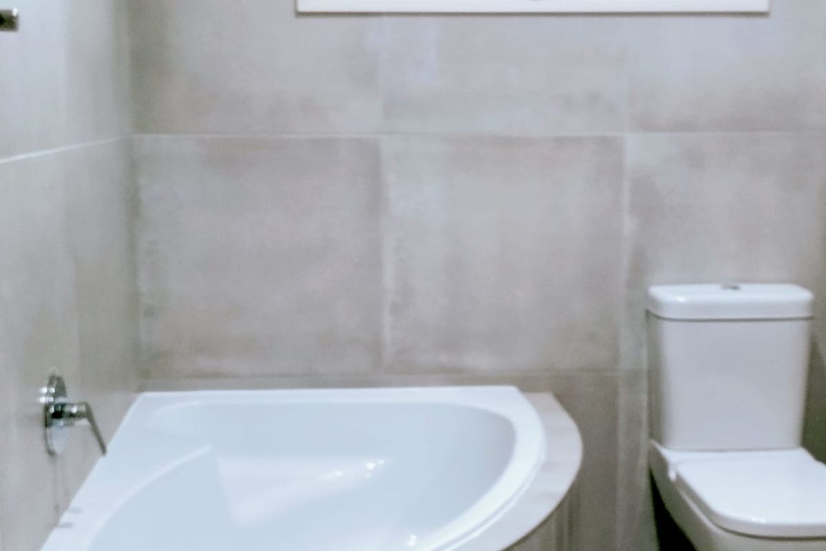 A modern bathroom featuring a corner bathtub, a white toilet, and neutral wall tiling with a window for natural light.