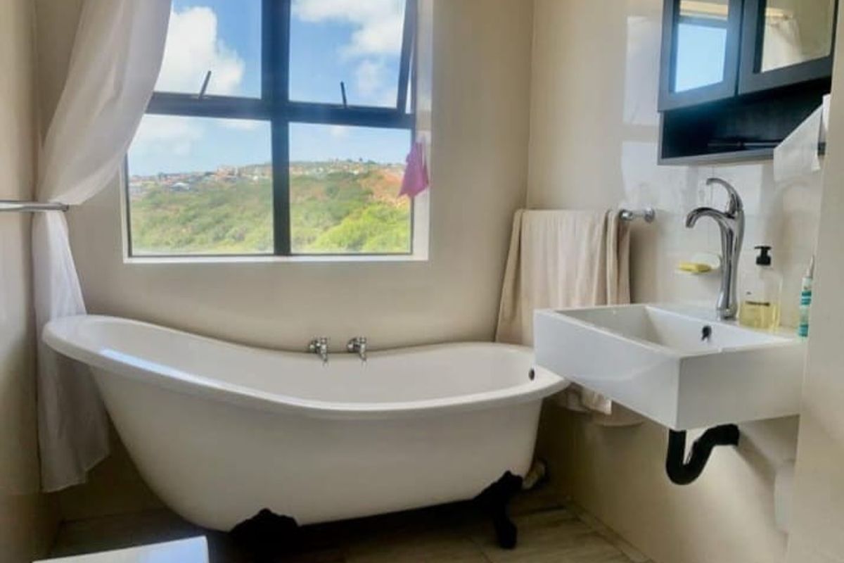 A bright bathroom featuring a freestanding clawfoot bathtub, a modern wall-mounted basin, and a large window offering scenic views.