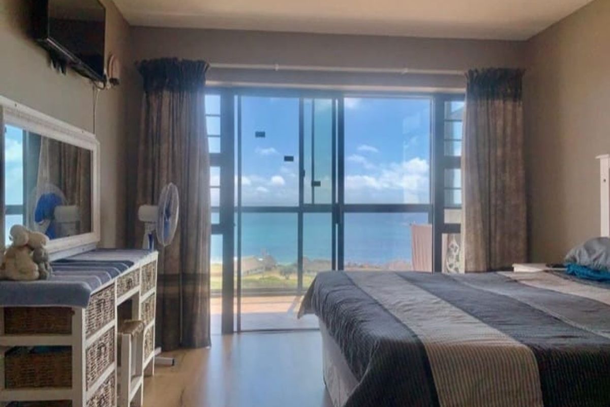 A bedroom featuring large sliding glass doors that open to a balcony with expansive ocean views, providing natural light and a coastal outlook.