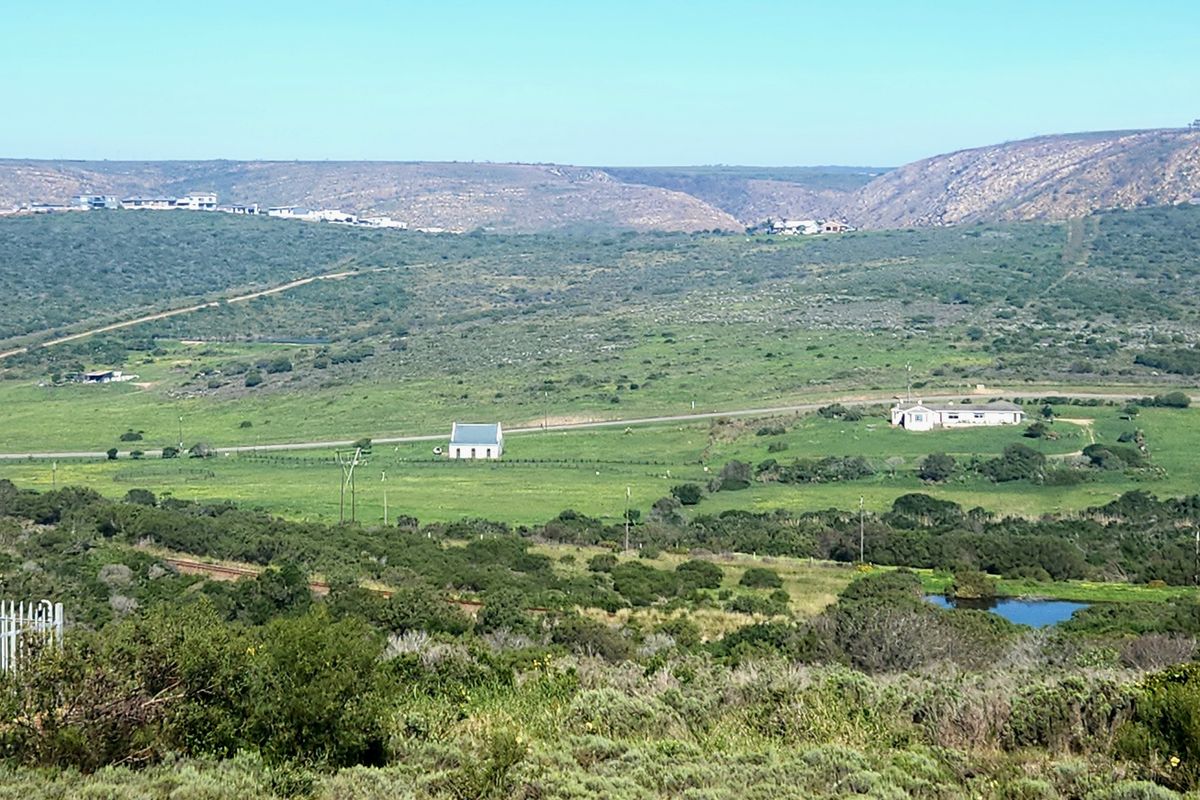 A wide-angle aerial view of a rural landscape featuring rolling green hills, open fields, and distant residential structures.