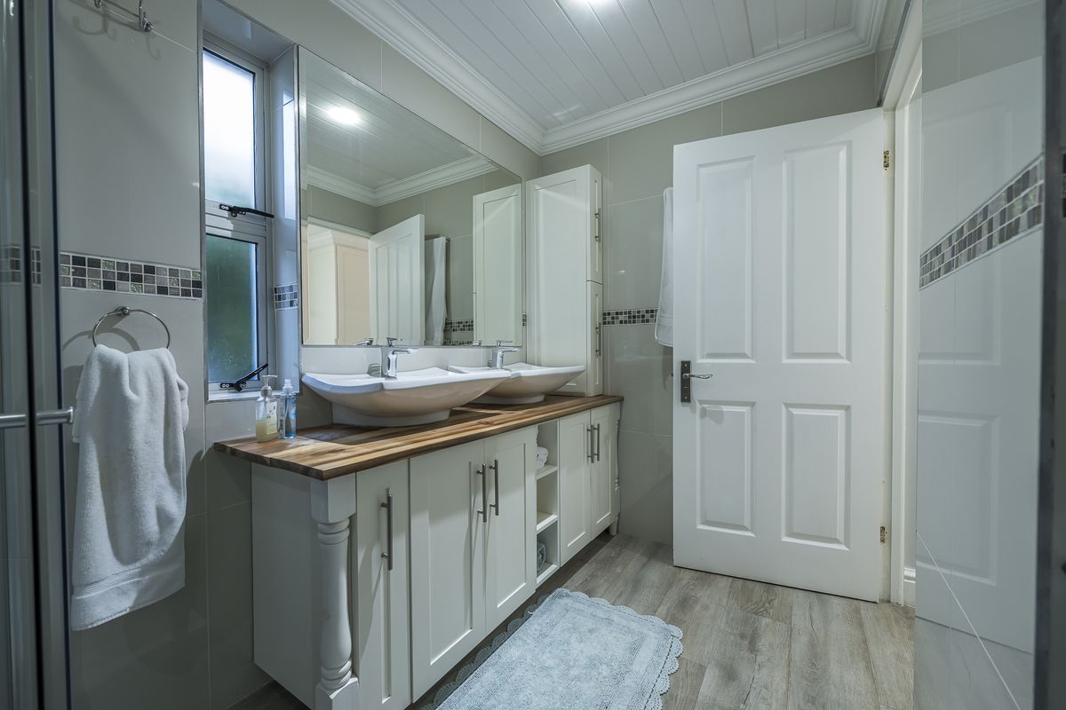 Modern bathroom featuring a double vanity with vessel sinks, wooden countertop, large wall mirror, and tiled walls with decorative mosaic accents.