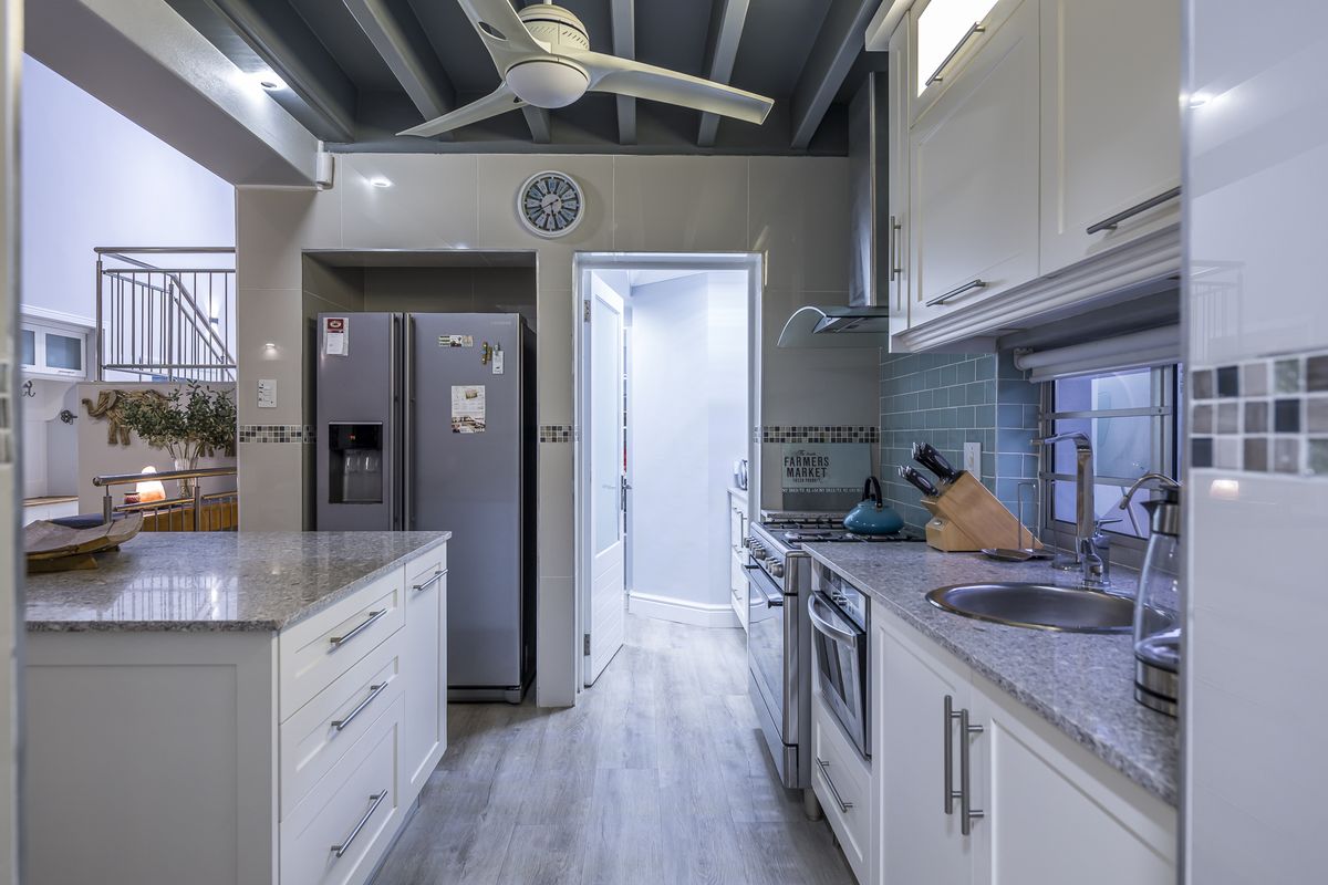 Modern kitchen featuring white cabinetry, granite countertops, subway tile backsplash, stainless steel gas range, extractor fan, and a ceiling fan.