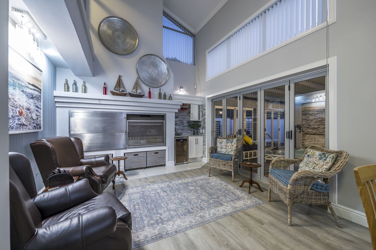 Spacious living area featuring a built-in indoor braai, high vaulted ceilings, and large glass sliding doors opening to the outdoor patio area.