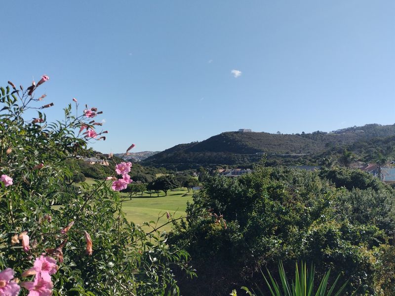 A scenic elevated view overlooking a lush green landscape and rolling hills under a clear blue sky.