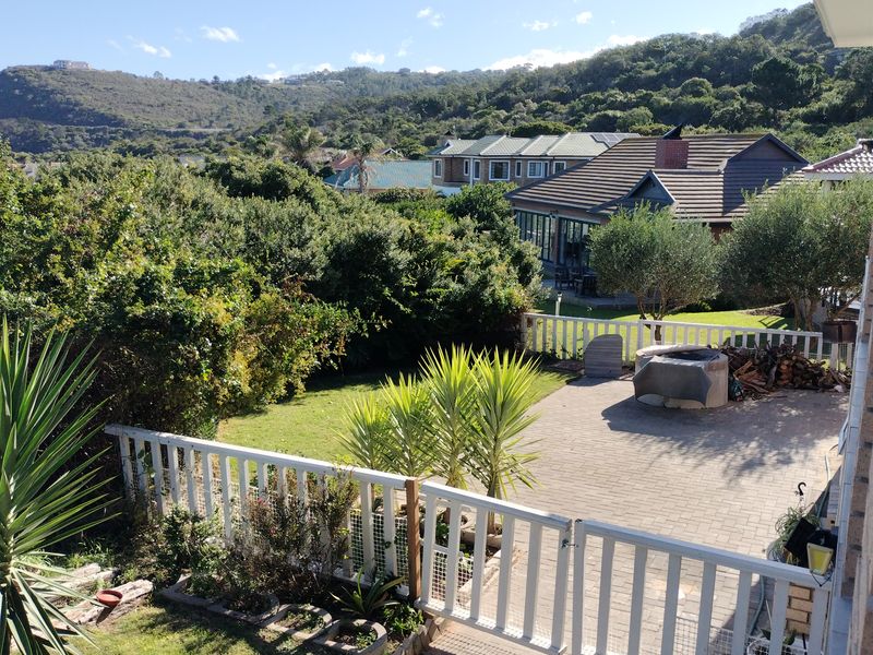 A spacious rear garden featuring a paved patio area with a built-in braai, enclosed by a white picket fence, overlooking a scenic landscape.