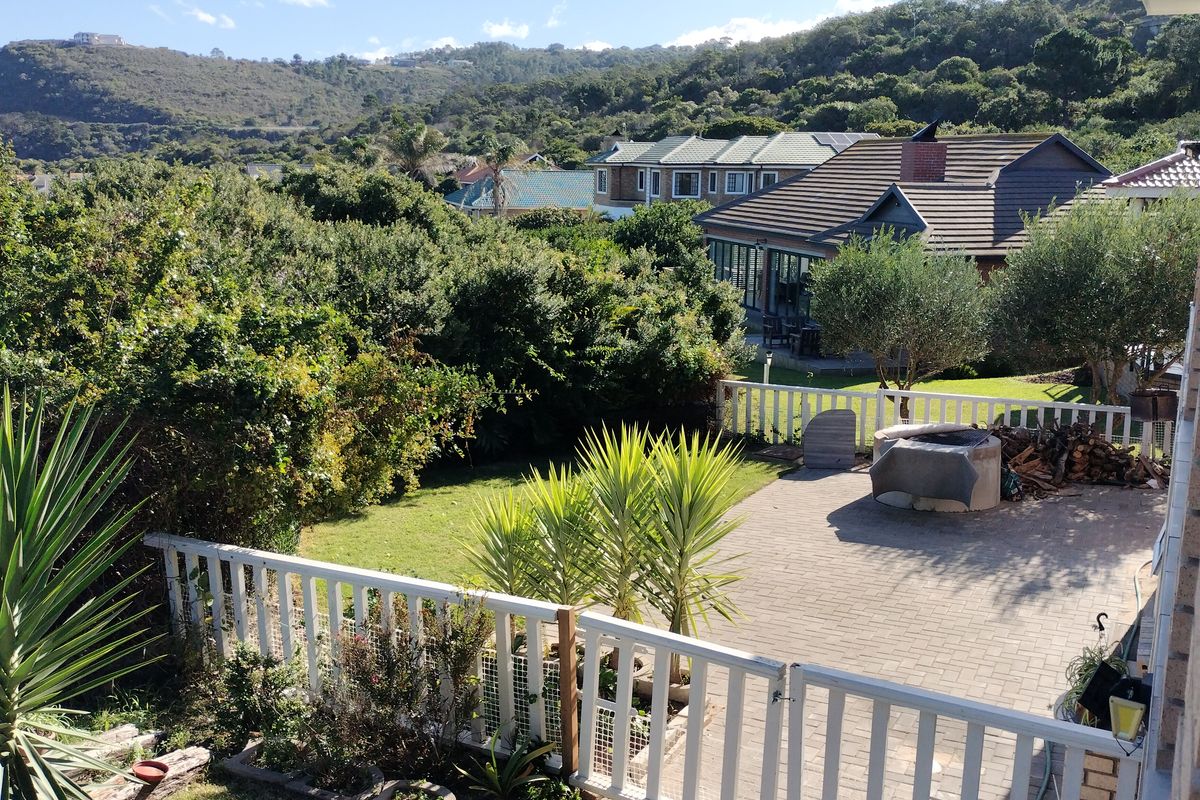 A spacious rear garden featuring a paved patio area with a built-in braai, enclosed by a white picket fence, overlooking a scenic landscape.