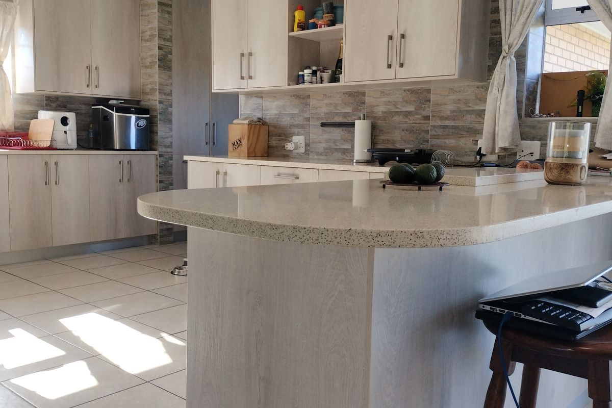 A functional kitchen featuring light-toned laminate cabinetry, stone-look countertops, a breakfast bar, and a tiled backsplash with ceramic flooring.