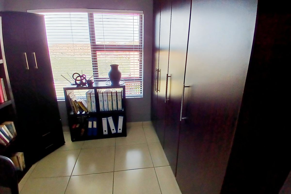 A functional bedroom or office space featuring built-in dark wood cabinetry and tiled flooring, illuminated by natural light through a window with blinds.