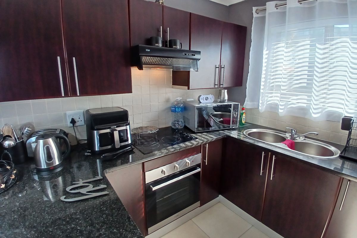 A functional kitchen featuring dark wood cabinetry, granite countertops, a built-in oven, electric hob, extractor fan, and a double stainless steel sink.