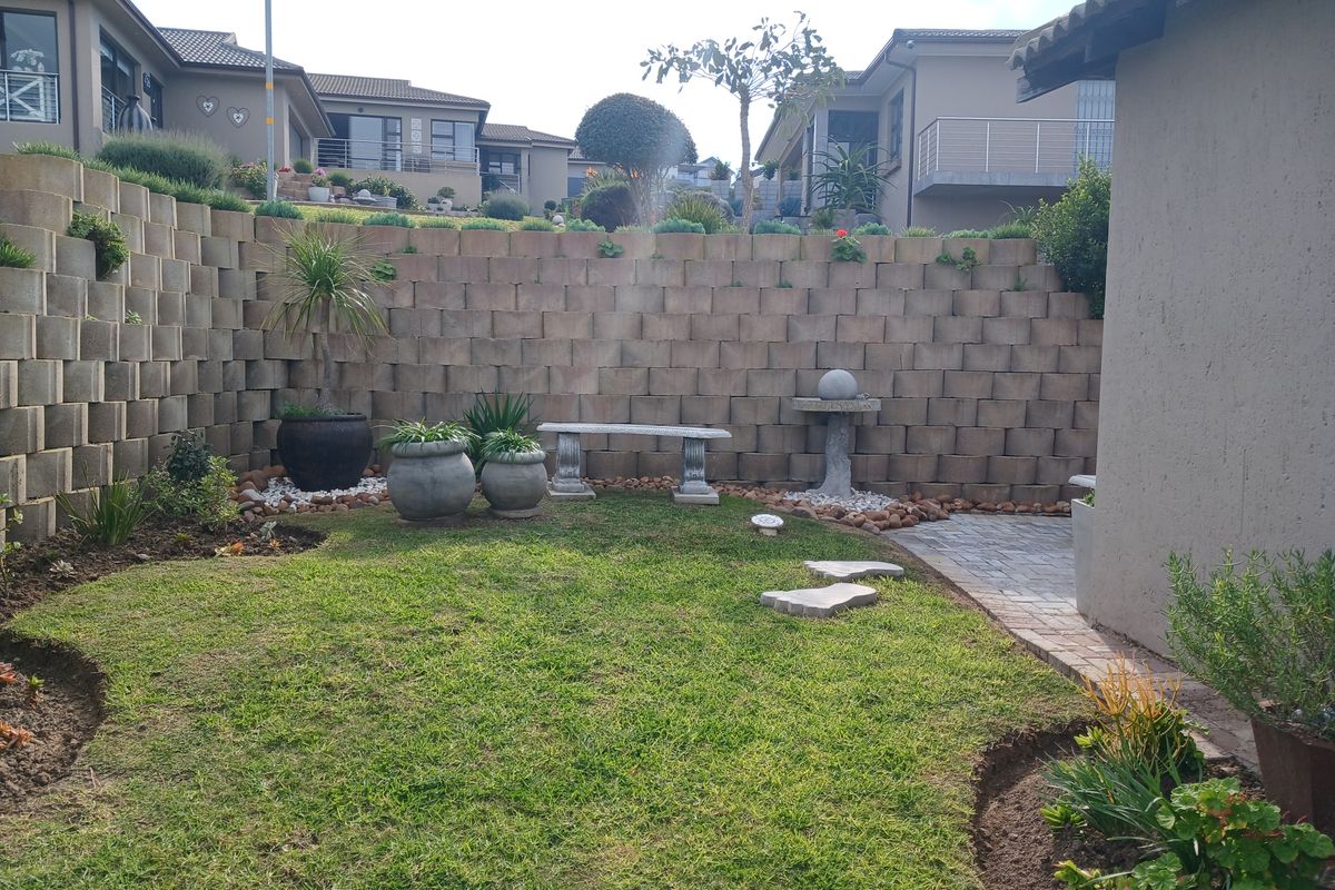 A well-maintained rear garden featuring a tiered concrete block retaining wall, paved walkway, and established lawn area.