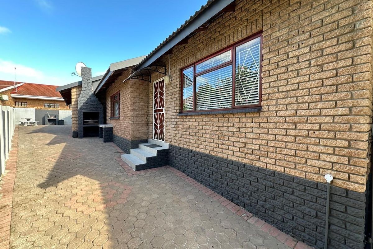 A view of the rear exterior featuring a paved courtyard, brick facade, and a built-in outdoor braai area.