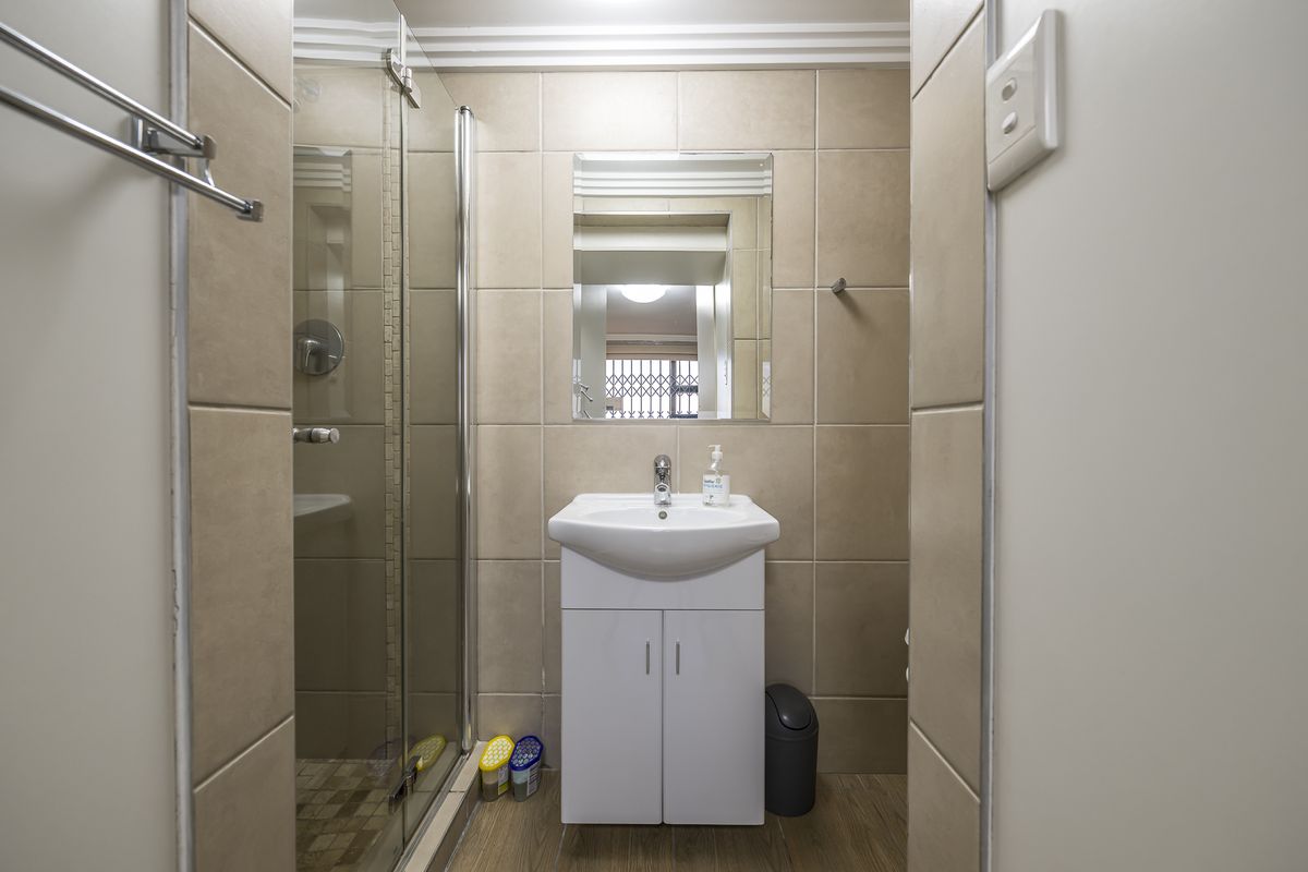 A compact bathroom featuring a glass-enclosed shower, a wall-mounted mirror, and a modern vanity basin with tiled walls and flooring.