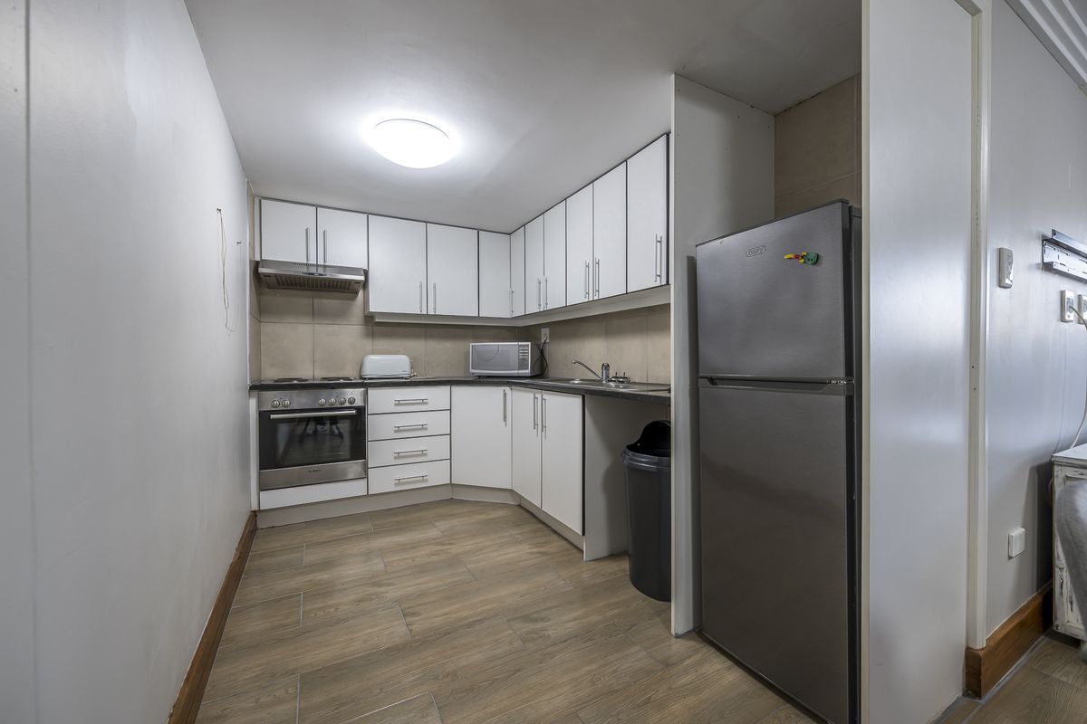 Compact kitchen featuring white cabinetry, laminate countertops, built-in oven, hob, and extractor fan with wood-look tiled flooring.