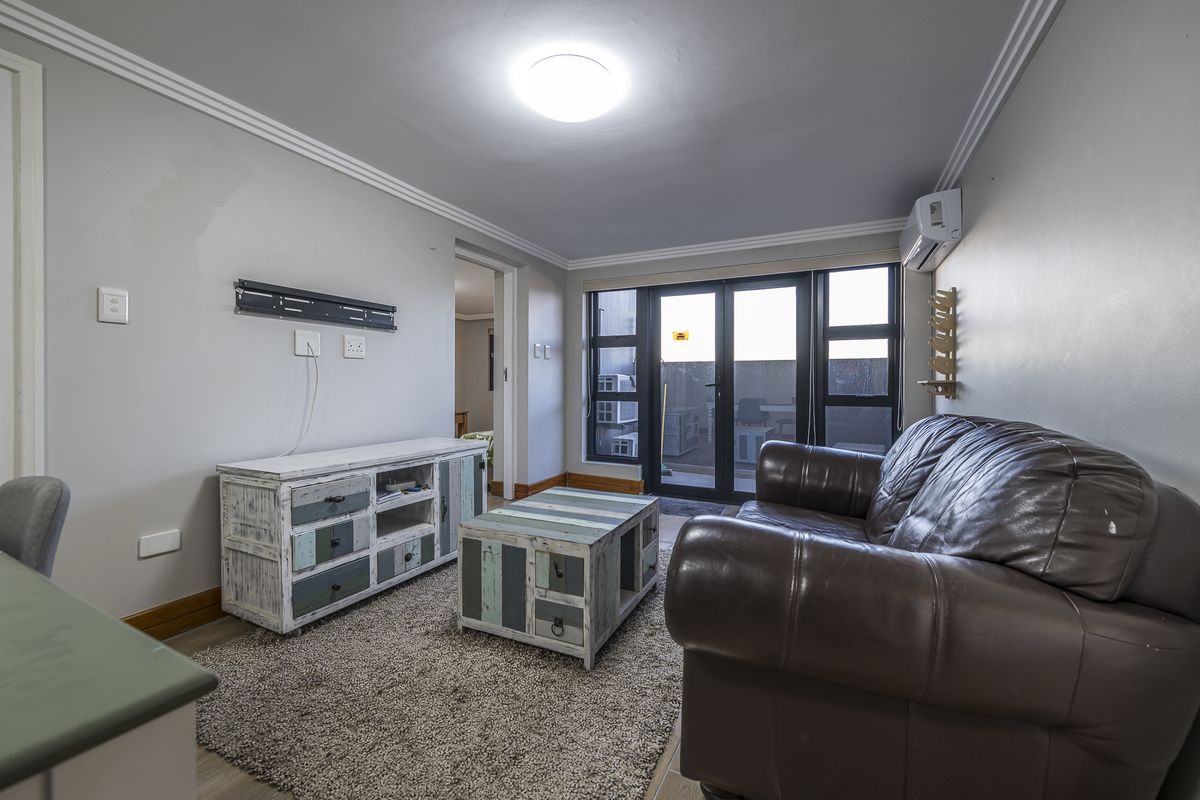 A living room featuring crown molding, a wall-mounted air conditioning unit, and large glass sliding doors leading to an outdoor area.