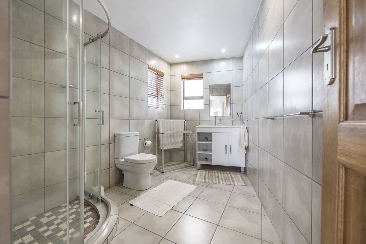 A modern bathroom featuring floor-to-ceiling neutral tiling, a glass-enclosed corner shower, a white vanity cabinet with integrated basin, and a toilet.