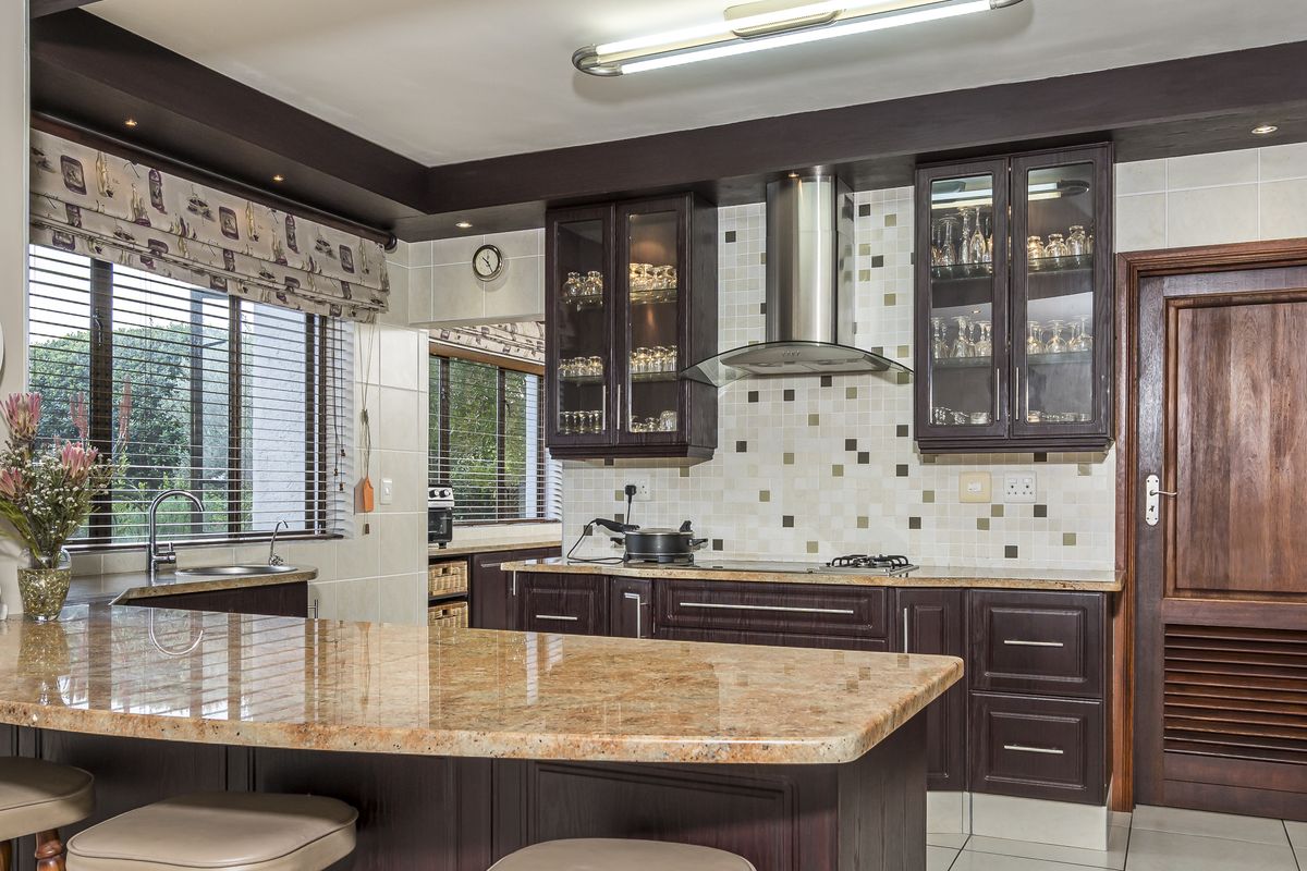 A well-maintained kitchen featuring dark wood cabinetry, granite countertops, a mosaic tile backsplash, stainless steel extractor fan, and a breakfast bar island.