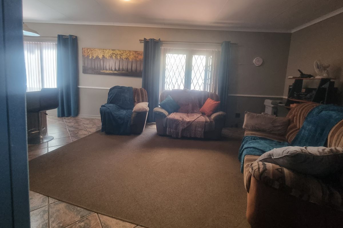 A spacious living room featuring tiled flooring, neutral wall tones, and large windows with security bars, providing a comfortable and functional living space.