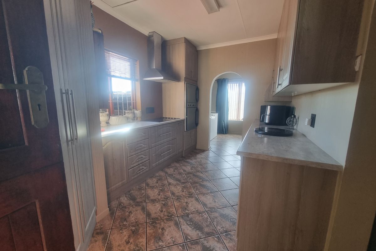 A functional kitchen featuring wood-look cabinetry, built-in oven, extractor fan, and tiled flooring, leading through an arched doorway to an adjacent space.