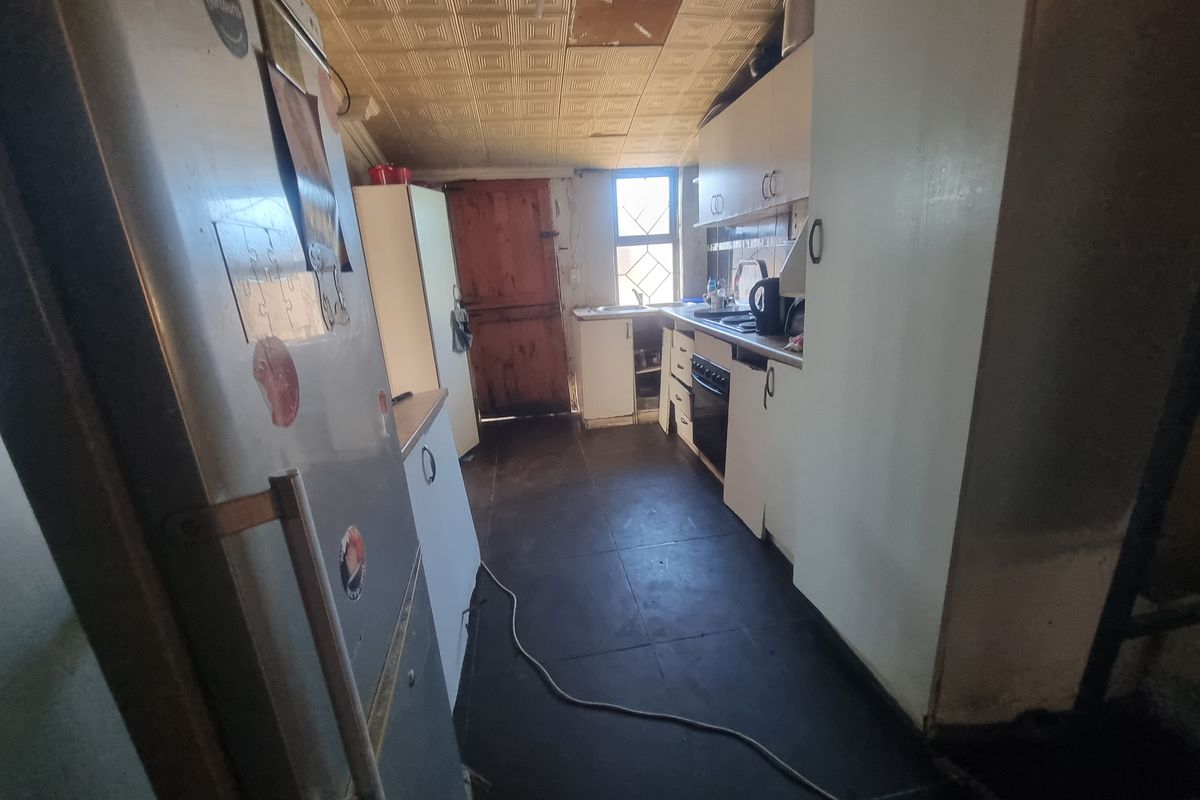 A dated kitchen featuring basic cabinetry, tiled flooring, and a textured ceiling, requiring significant renovation to modernize the space.