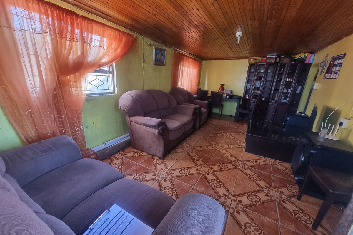 A living room featuring a wood-paneled ceiling and patterned ceramic floor tiles, providing a functional space with potential for cosmetic updates.