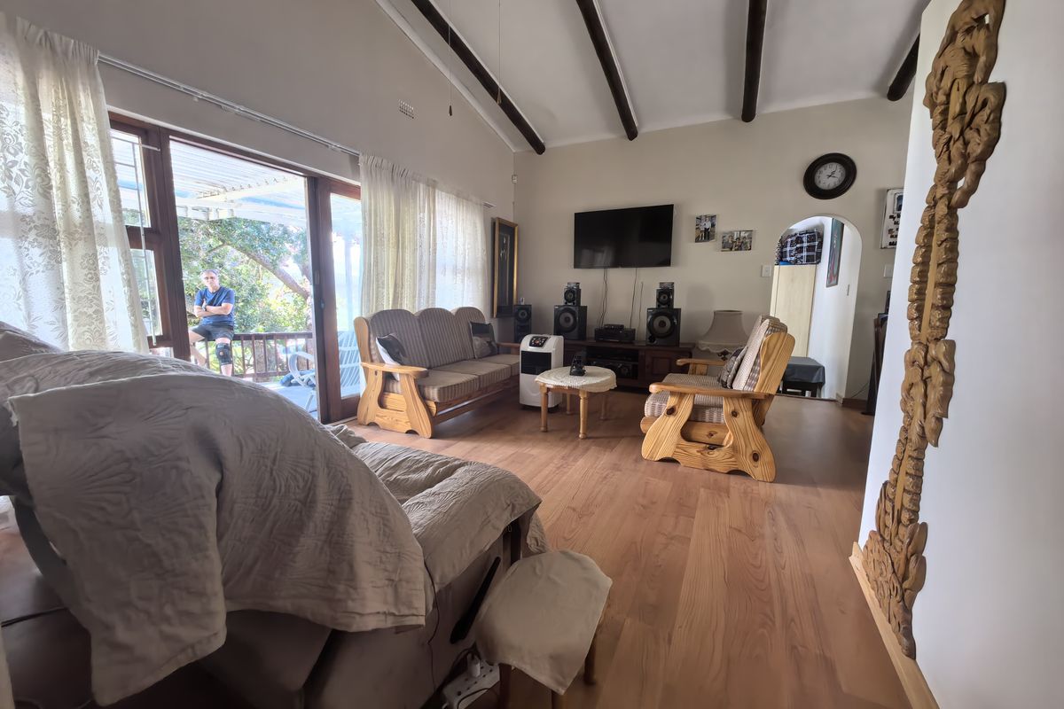 Spacious living room featuring vaulted ceilings with exposed timber beams, laminate flooring, and large sliding glass doors providing access to the outdoor patio area.
