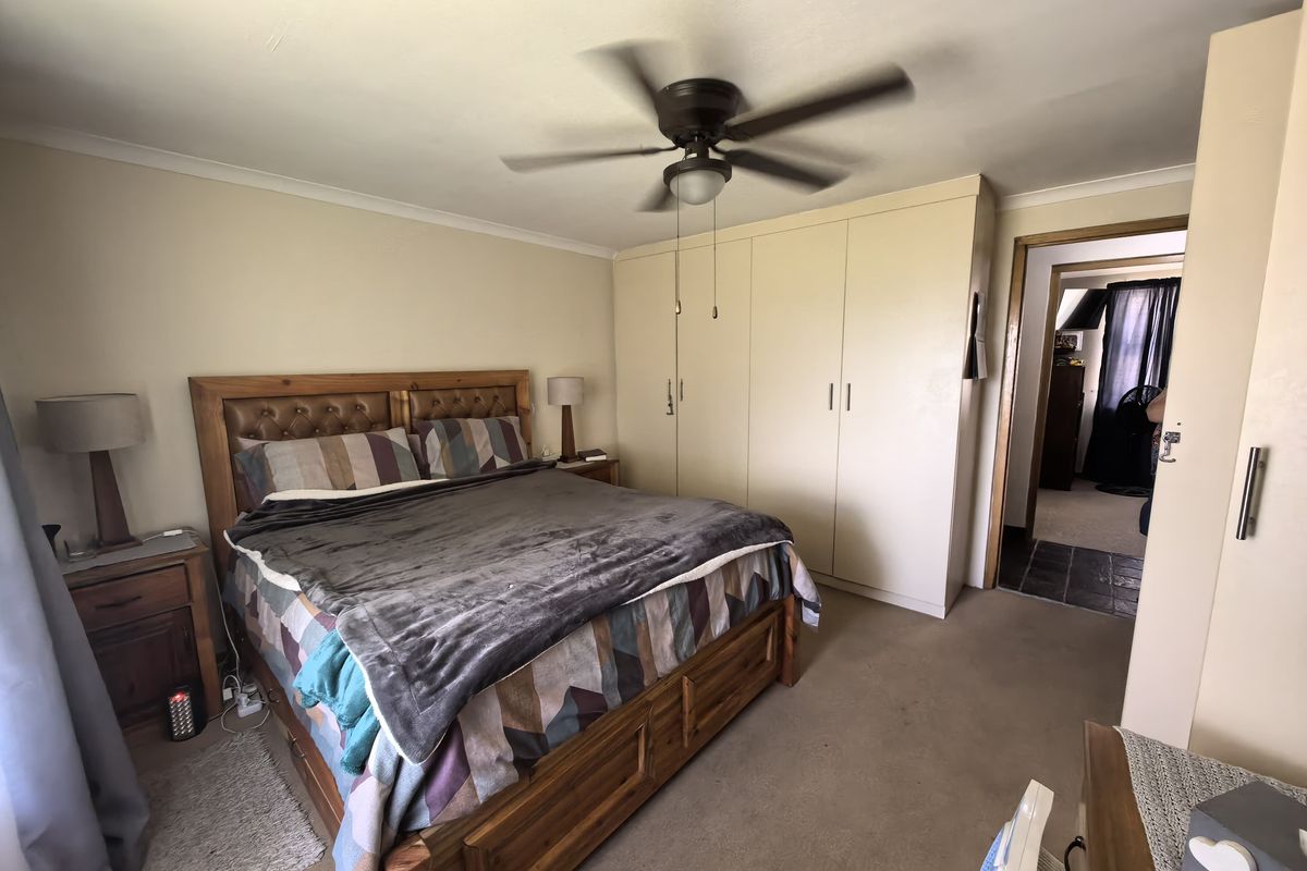 A bedroom featuring built-in floor-to-ceiling wardrobes, a ceiling fan, and carpeted flooring, with an adjacent doorway leading to another room.