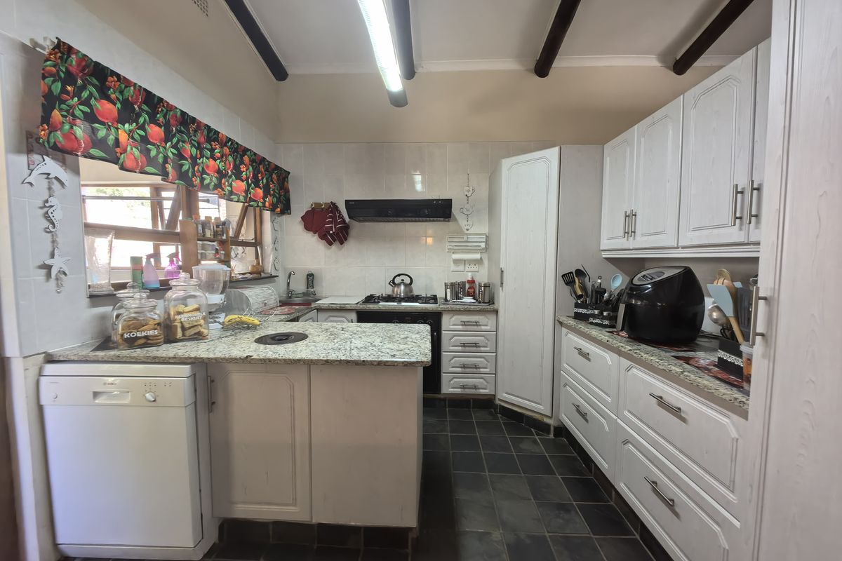 A functional kitchen featuring white cabinetry, granite countertops, a built-in gas hob, extractor fan, and dark slate floor tiles.