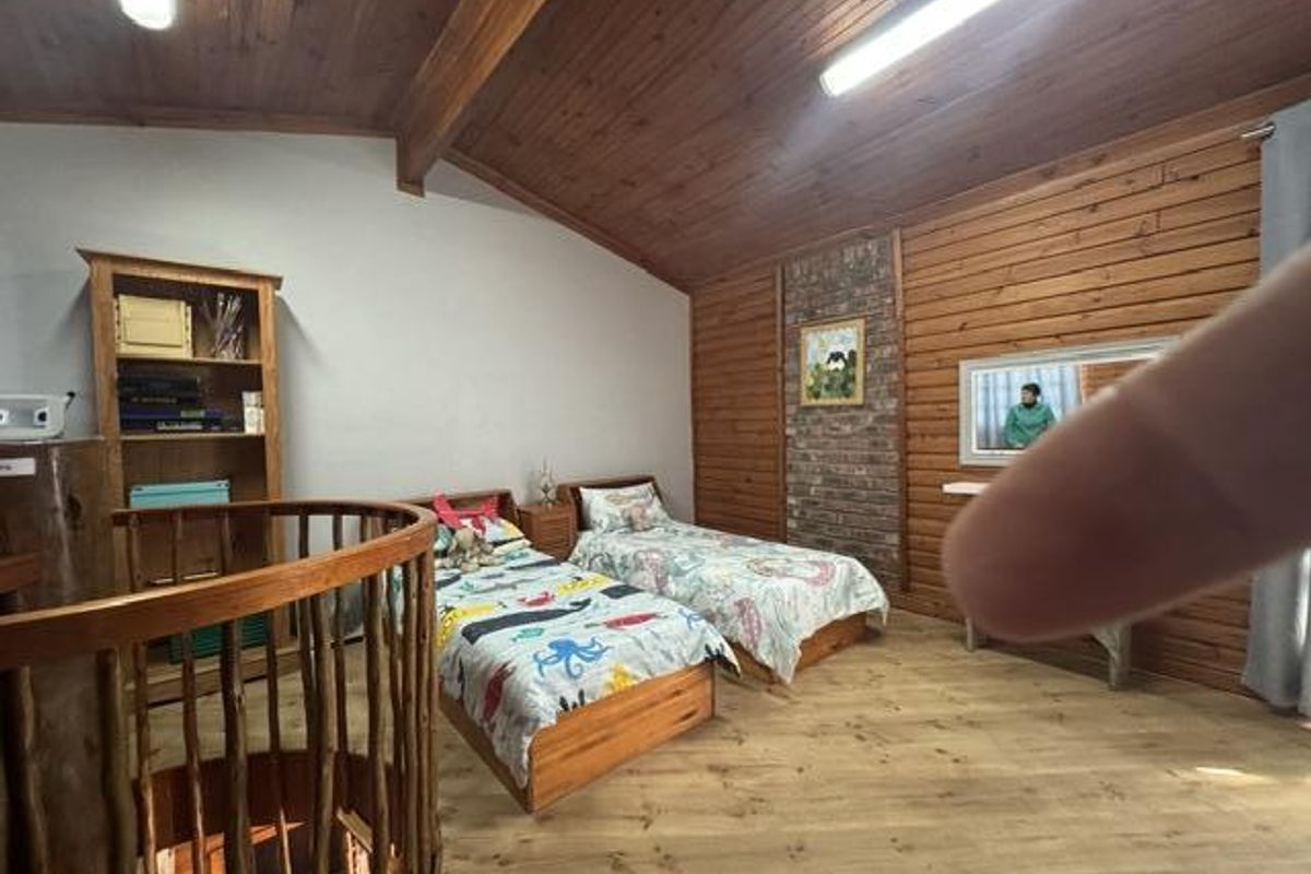 A bedroom featuring a vaulted timber-clad ceiling, wood-paneled feature wall, brick chimney breast, and a spiral staircase leading to the lower level.