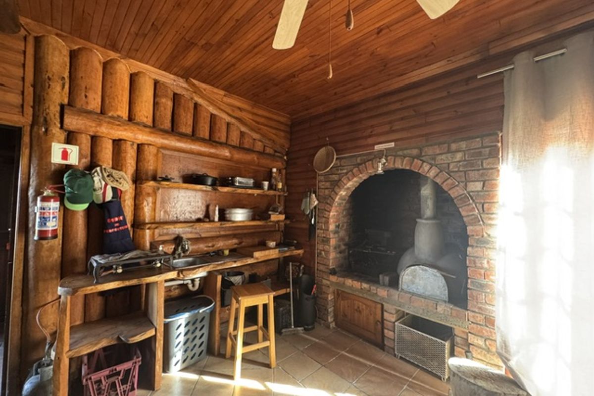 Rustic kitchen area featuring exposed log walls, timber ceiling, and a traditional brick-built fireplace with integrated oven.
