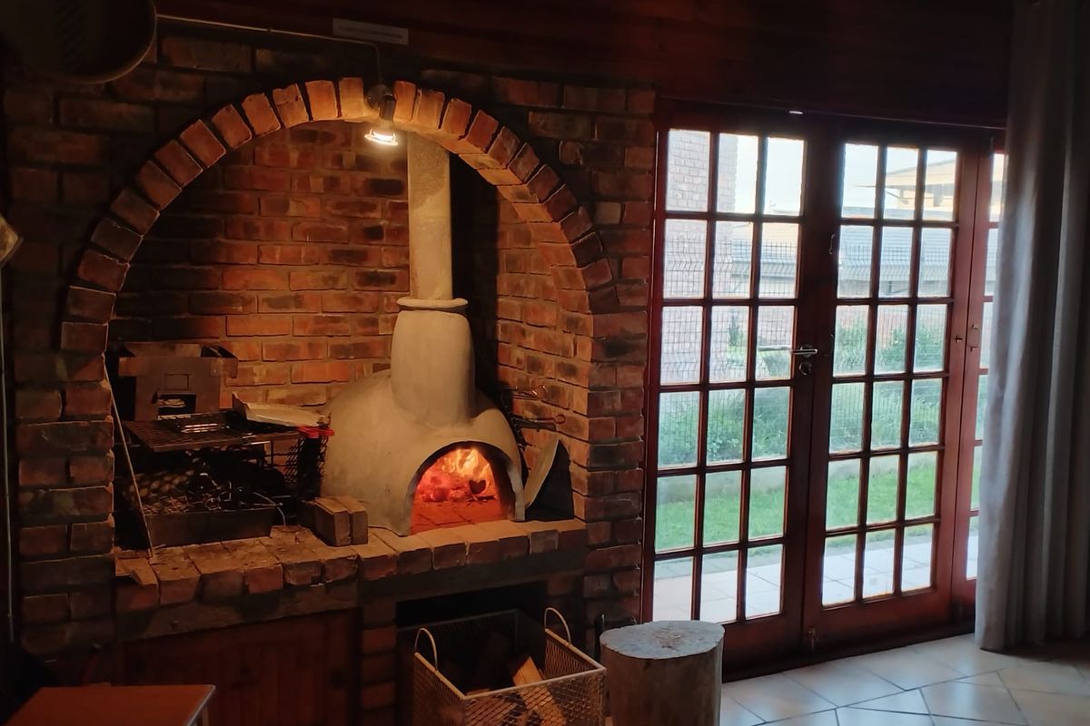 Indoor entertainment area featuring a rustic brick-built fireplace and pizza oven, with French doors leading to the garden.