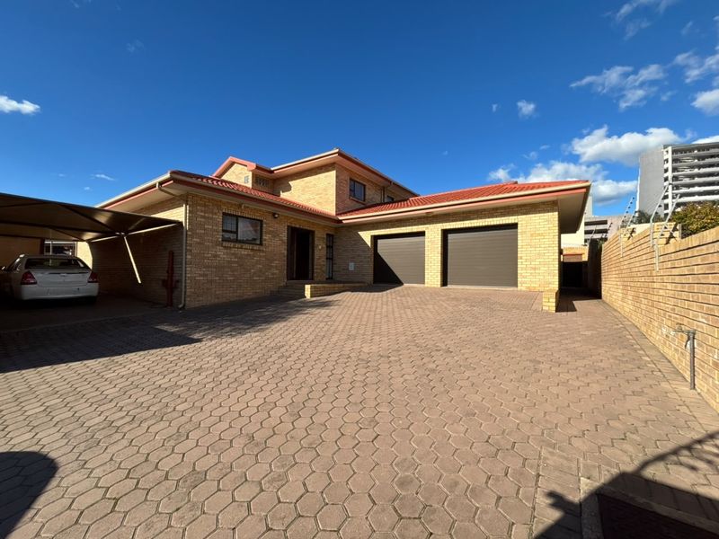 Front exterior view of a brick house featuring a double garage, paved driveway, and an attached carport.