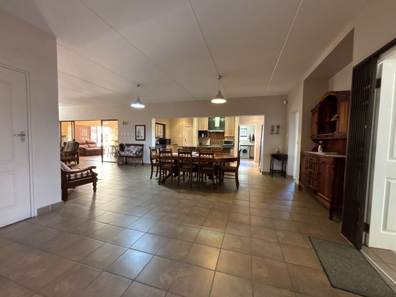 Spacious open-plan living and dining area featuring tiled flooring, pendant lighting, and a connected kitchen with built-in cabinetry and an extractor fan.
