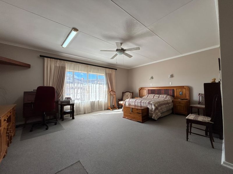 Spacious bedroom featuring neutral wall tones, carpeted flooring, a ceiling fan, and wall-mounted lighting fixtures.