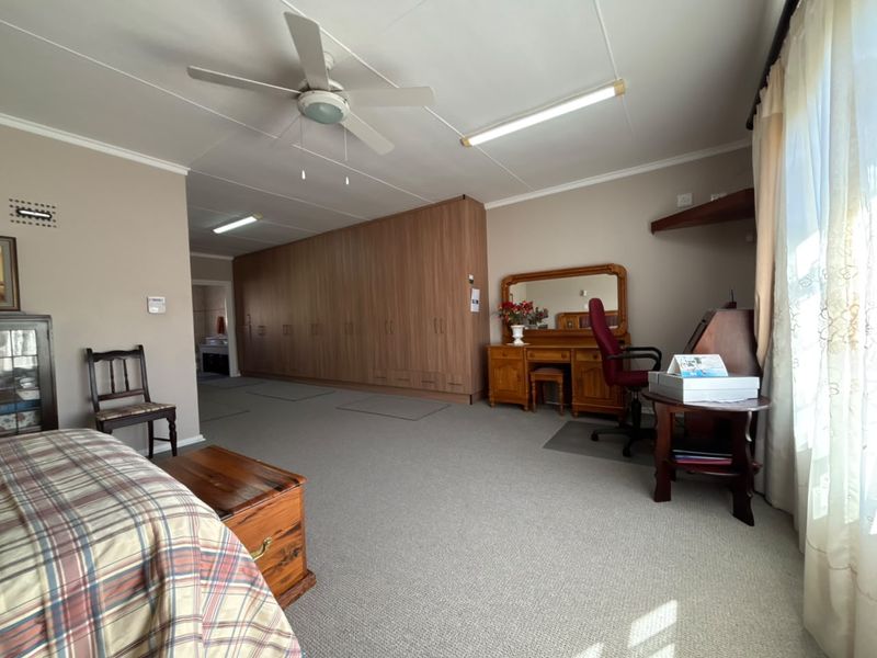 Spacious bedroom featuring extensive built-in cupboards, neutral carpeting, and a ceiling fan, offering ample storage and a functional layout.