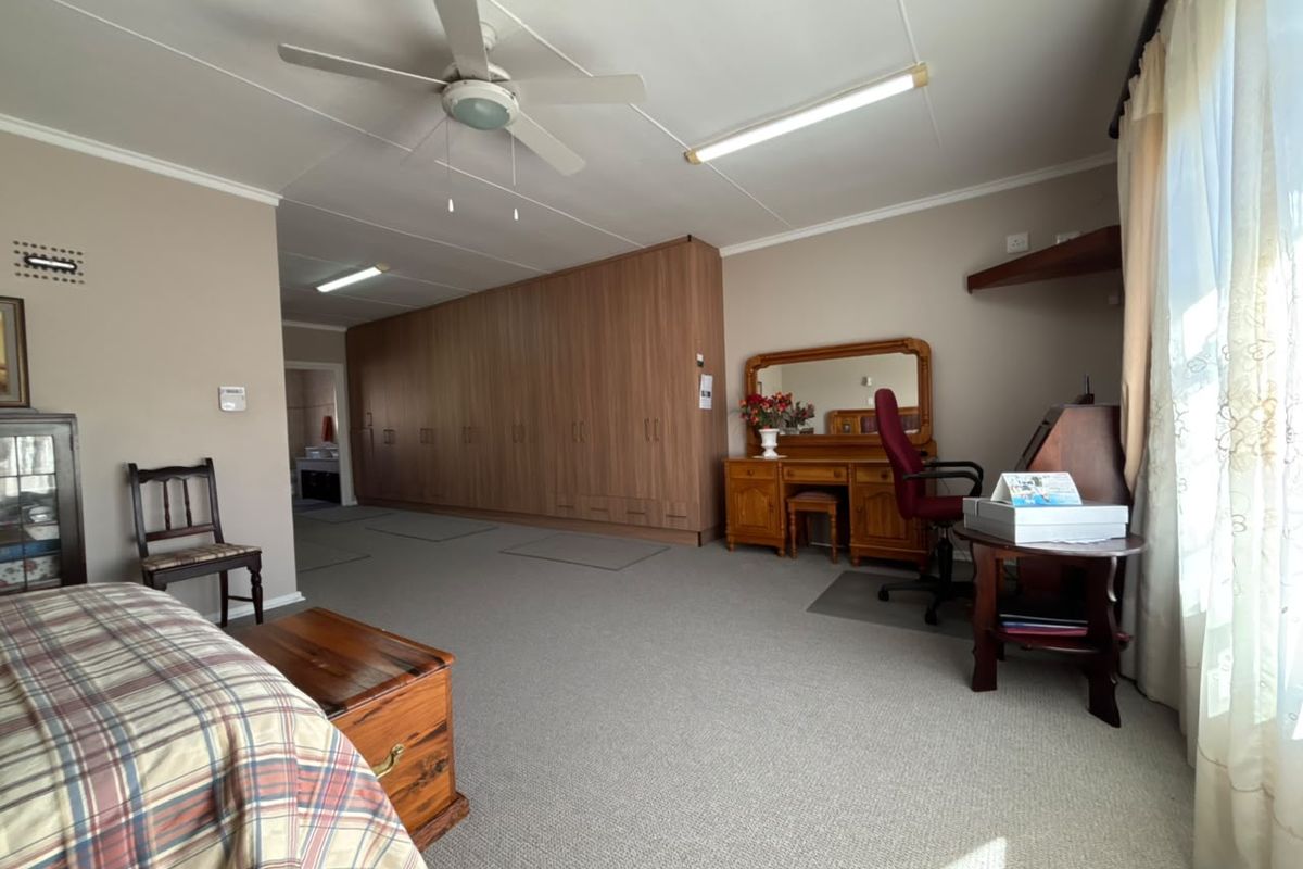 Spacious bedroom featuring extensive built-in cupboards, neutral carpeting, and a ceiling fan, offering ample storage and a functional layout.