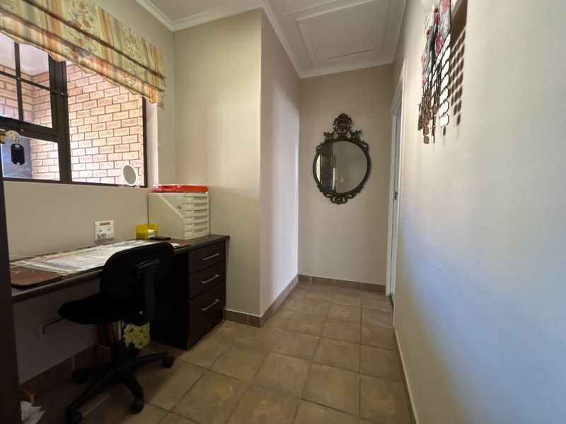 A functional home office space featuring tiled flooring, neutral walls, and a window with brickwork detailing.